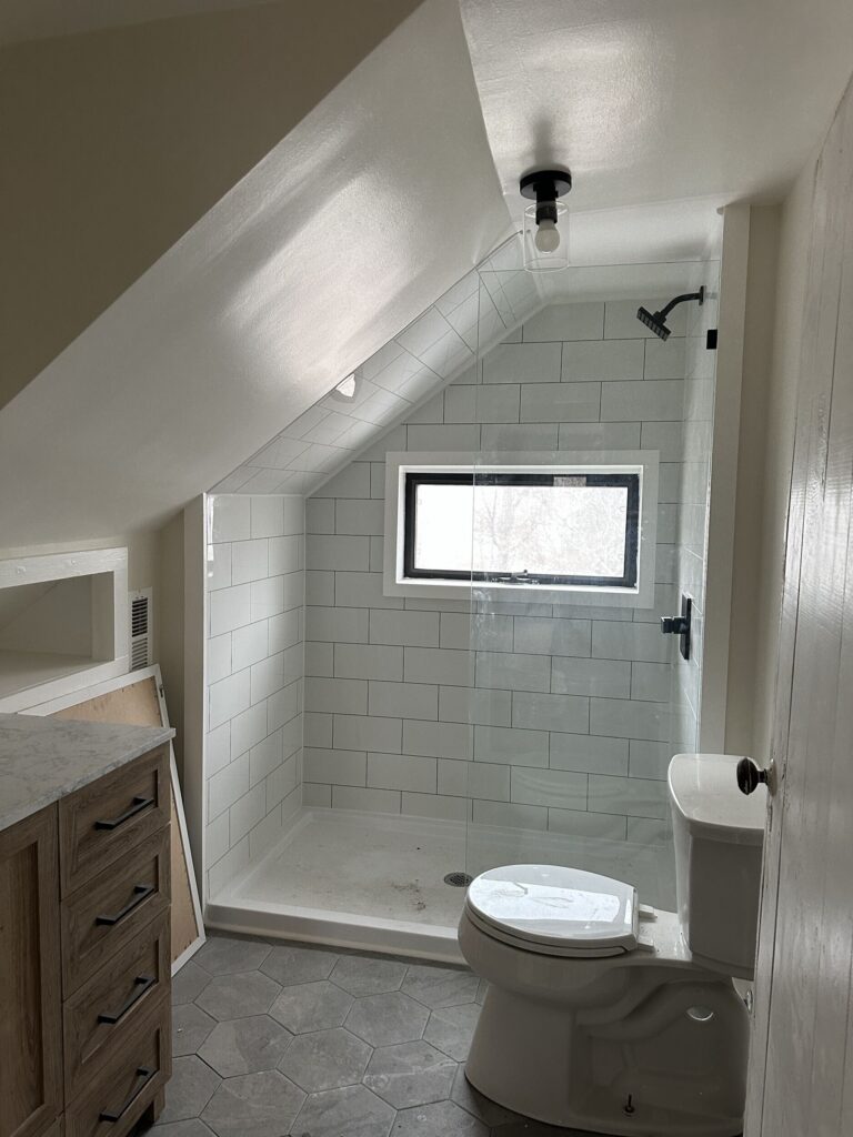 A remodeled bathroom featuring a shower, toilet, and sink, with neutral-colored tiles and modern fixtures.